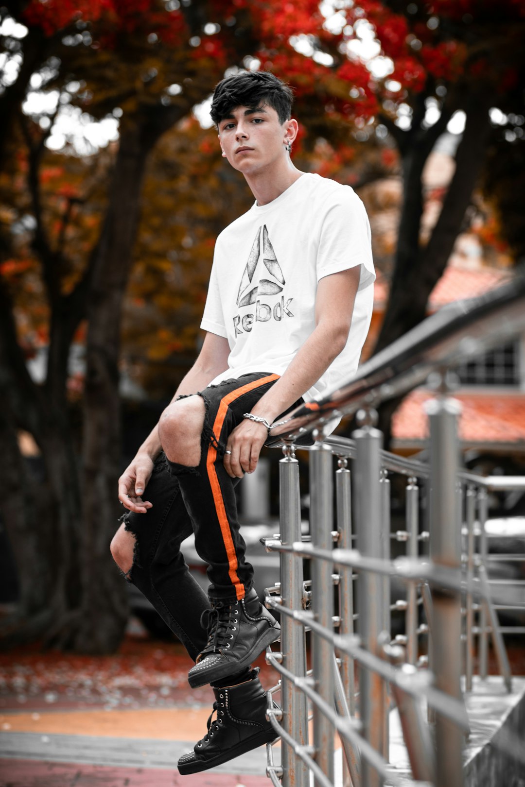 man in white crew neck t-shirt and black pants sitting on gray metal fence during