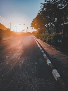 Quiet stretch of road disappearing into the golden light of sunset with distant mountains.