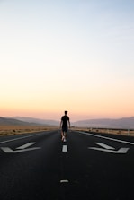 man in black jacket and black pants standing on black asphalt road during daytime