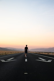man in black jacket and black pants standing on black asphalt road during daytime