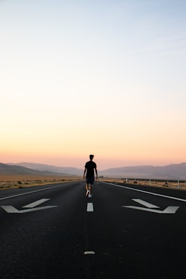man in black jacket and black pants standing on black asphalt road during daytime