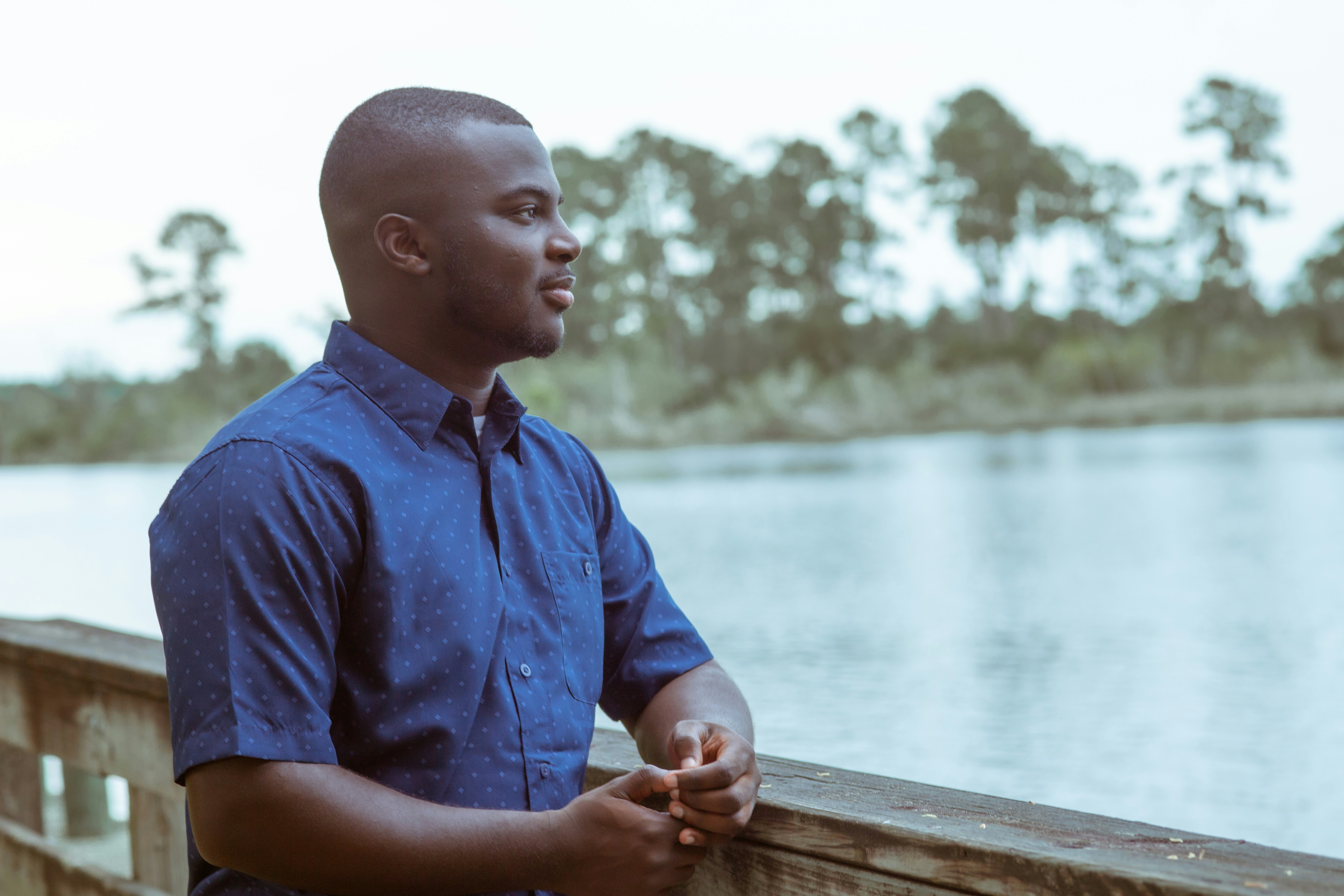 man in blue button up shirt sitting on brown wooden bench thoughtful teams background