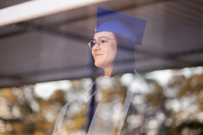 woman in blue academic gown wearing blue academic hat commencement teams background