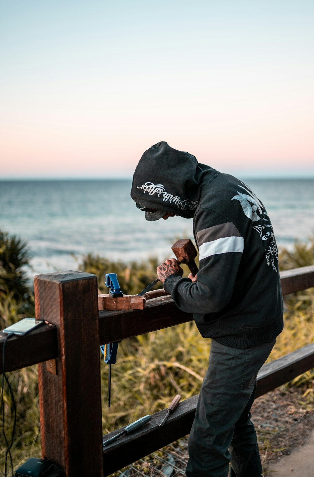 man in black and white hoodie and gray pants standing on brown wooden dock during daytime