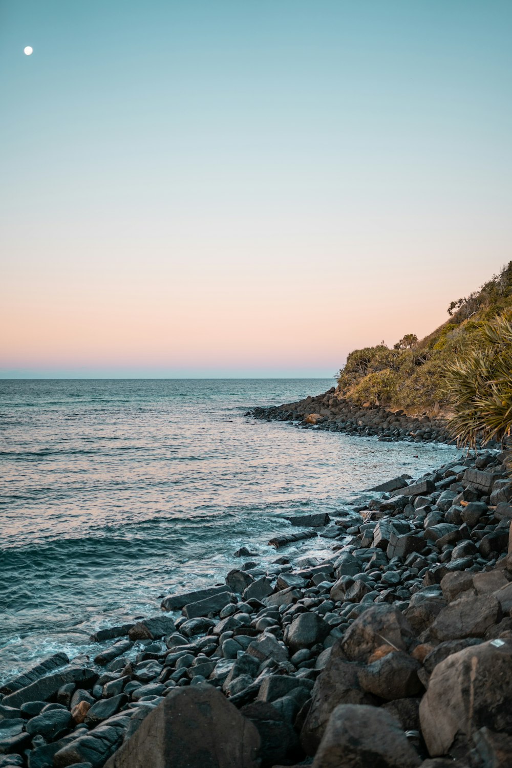 rocky shore with rocks and green grass under blue sky during daytime