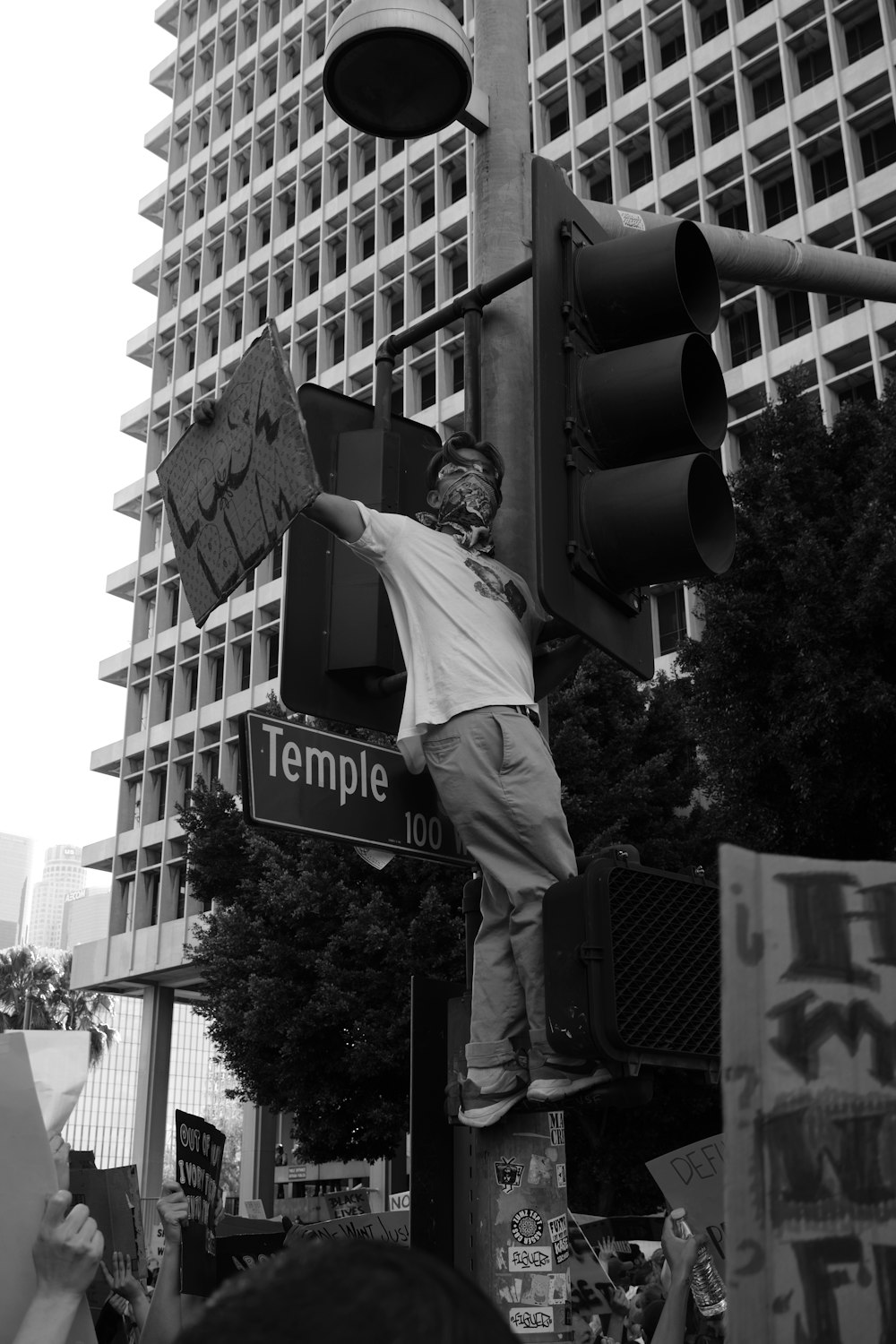 man in black suit jacket and pants standing on traffic light in grayscale photography