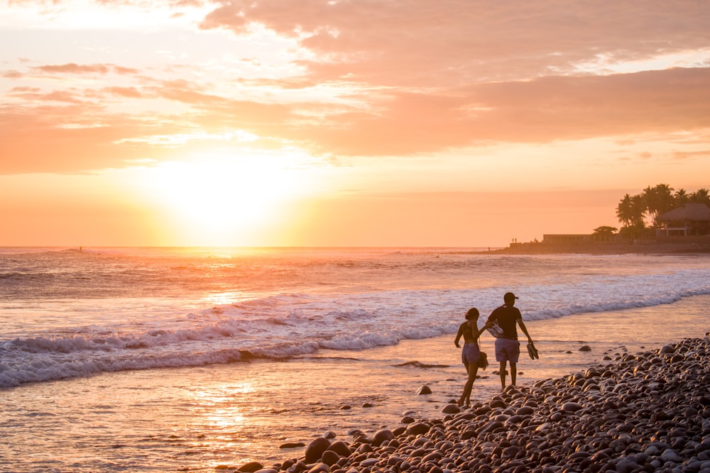 silhouette of 2 people standing on beach during sunset