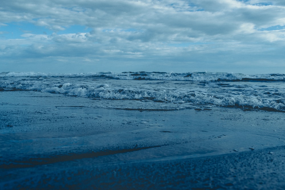 ocean waves crashing on shore under cloudy sky during daytime