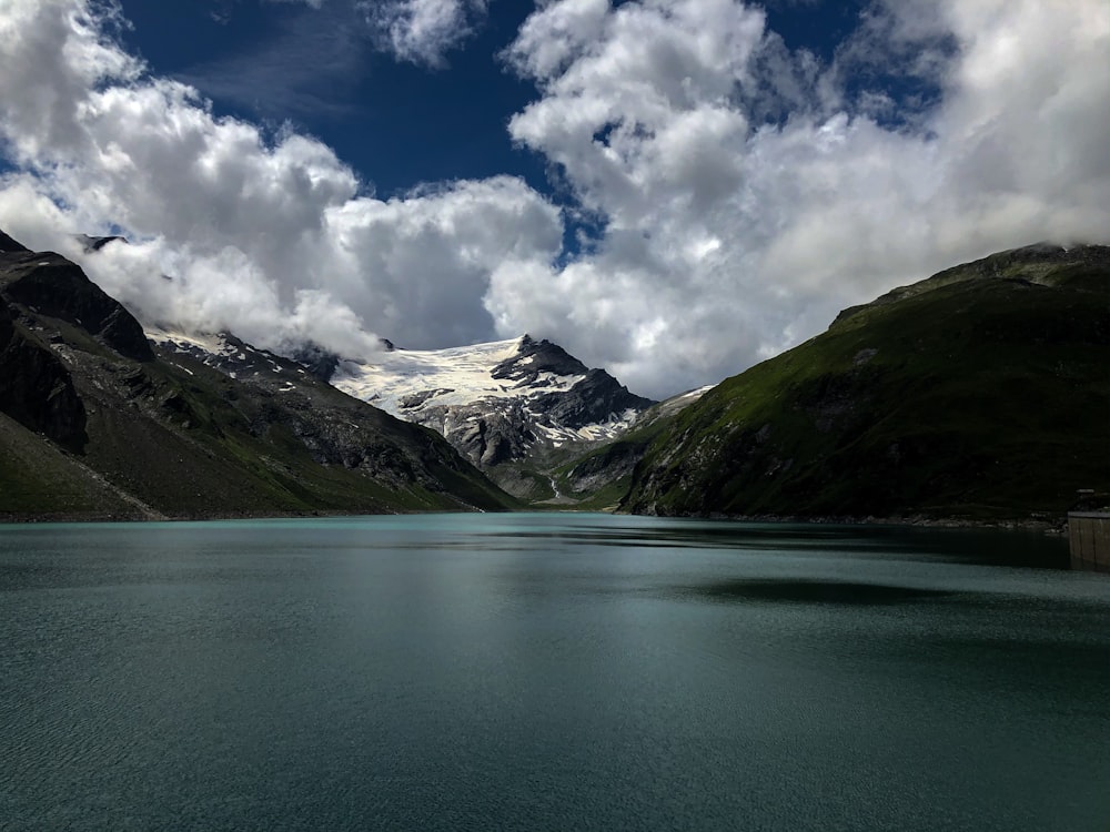 green lake near green mountains under blue and white cloudy sky during daytime