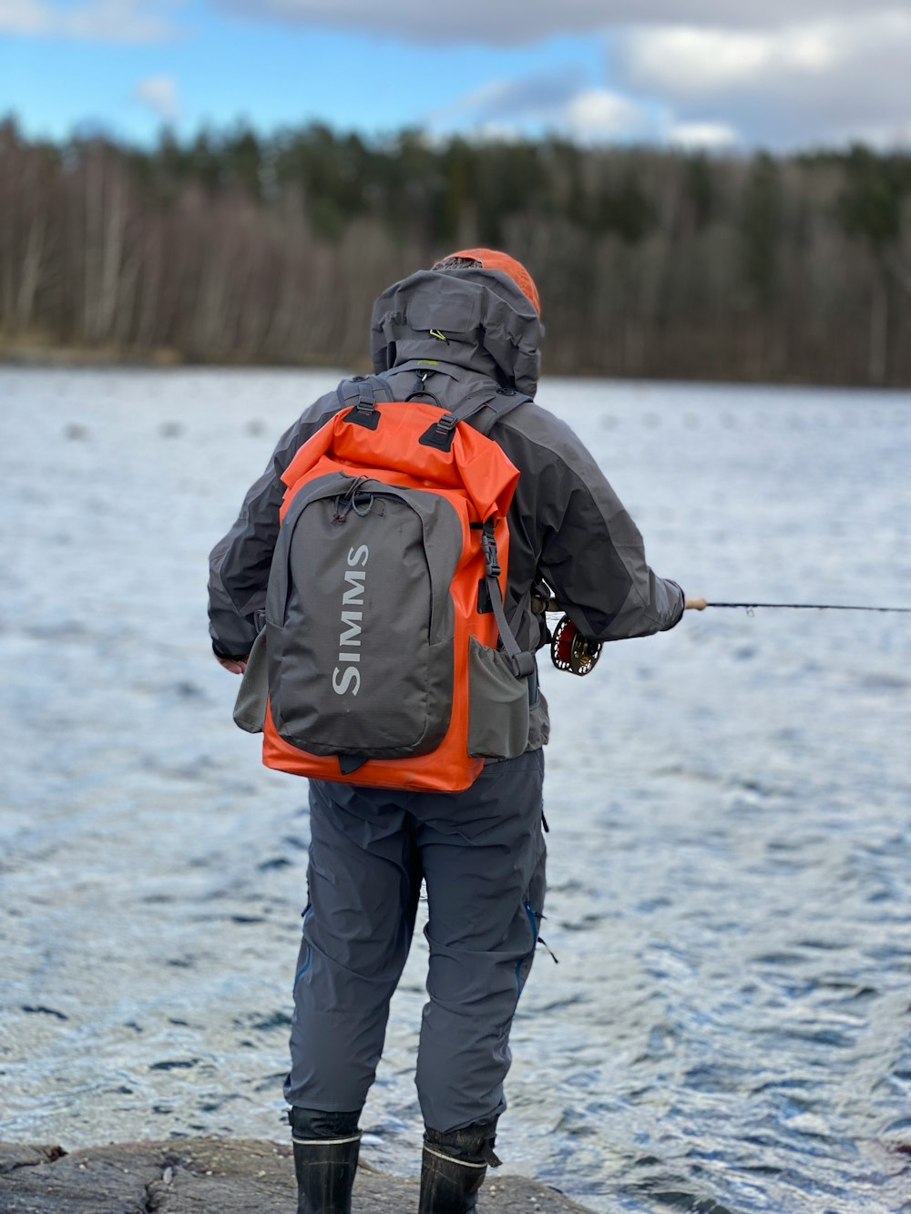 person in black and orange jacket and black pants holding black and white fishing rod