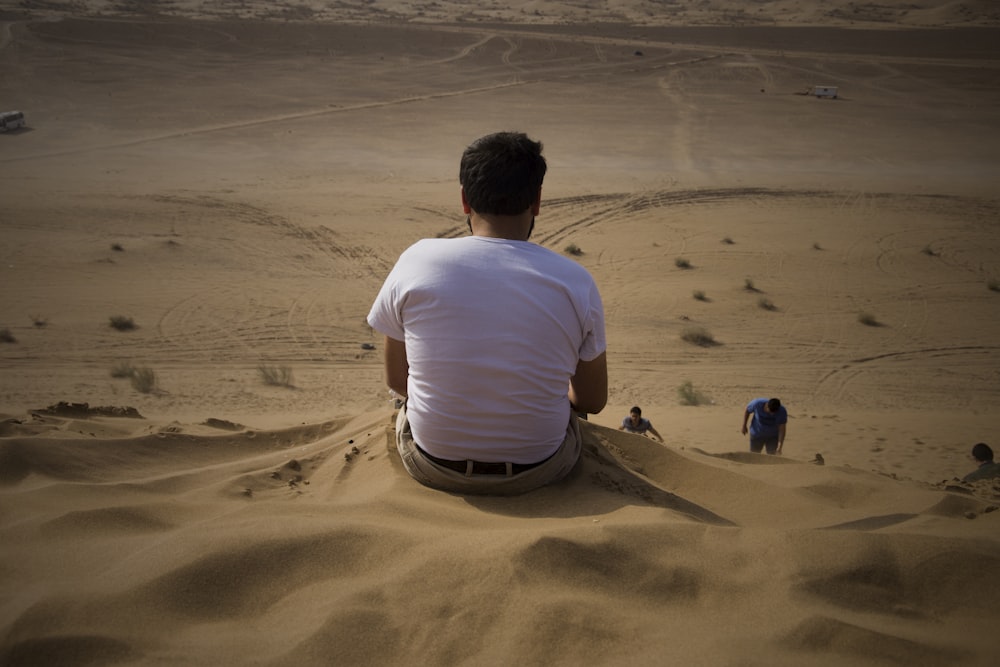 man in white t-shirt sitting on sand during daytime