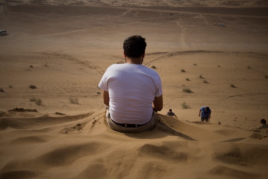 man in white t-shirt sitting on sand during daytime in Kashan Iran