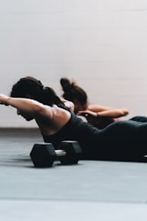 woman in black tank top and black leggings lying on black floor