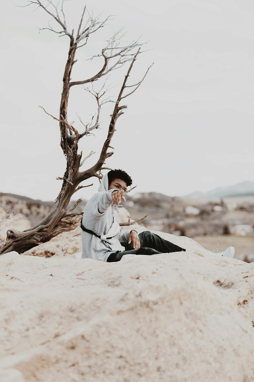 man in white dress shirt and black pants sitting on brown sand near brown bare tree