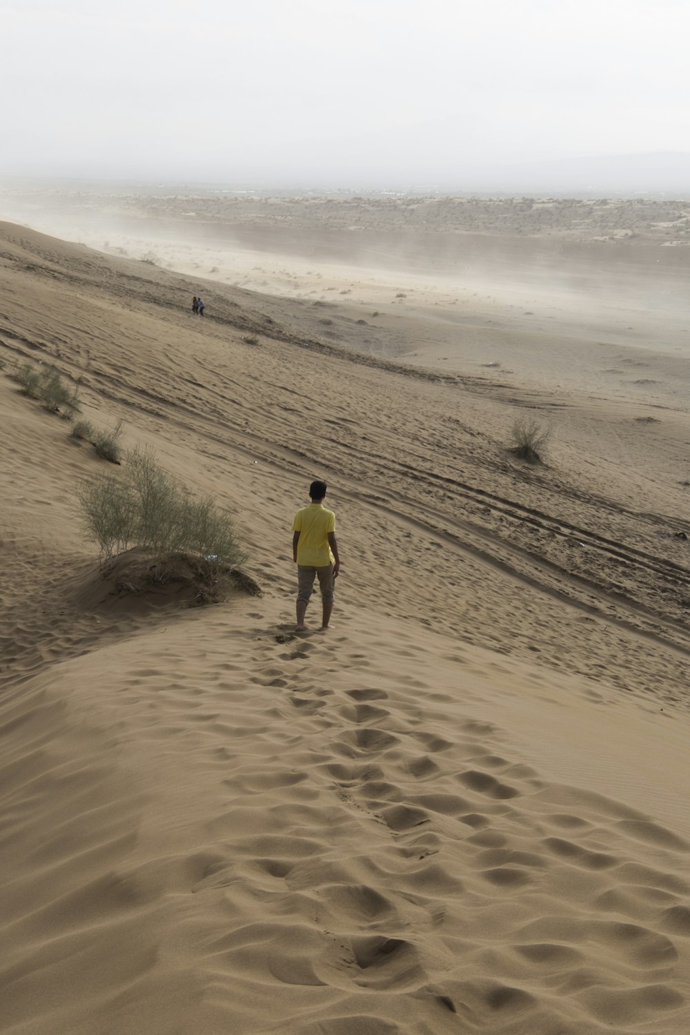 man in yellow shirt walking on brown sand during daytime