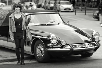 A smiling female driver in business attire standing beside her elegant car.
