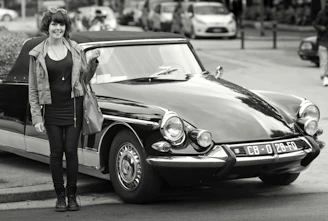 A plus-size model wearing a vintage V8 muscle car graphic tee, standing beside a classic red muscle car.