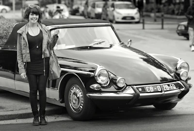 A smiling female driver in business attire standing beside her elegant car.