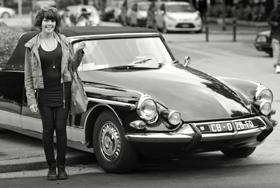 A plus-size model wearing a vintage V8 muscle car graphic tee, standing beside a classic red muscle car.