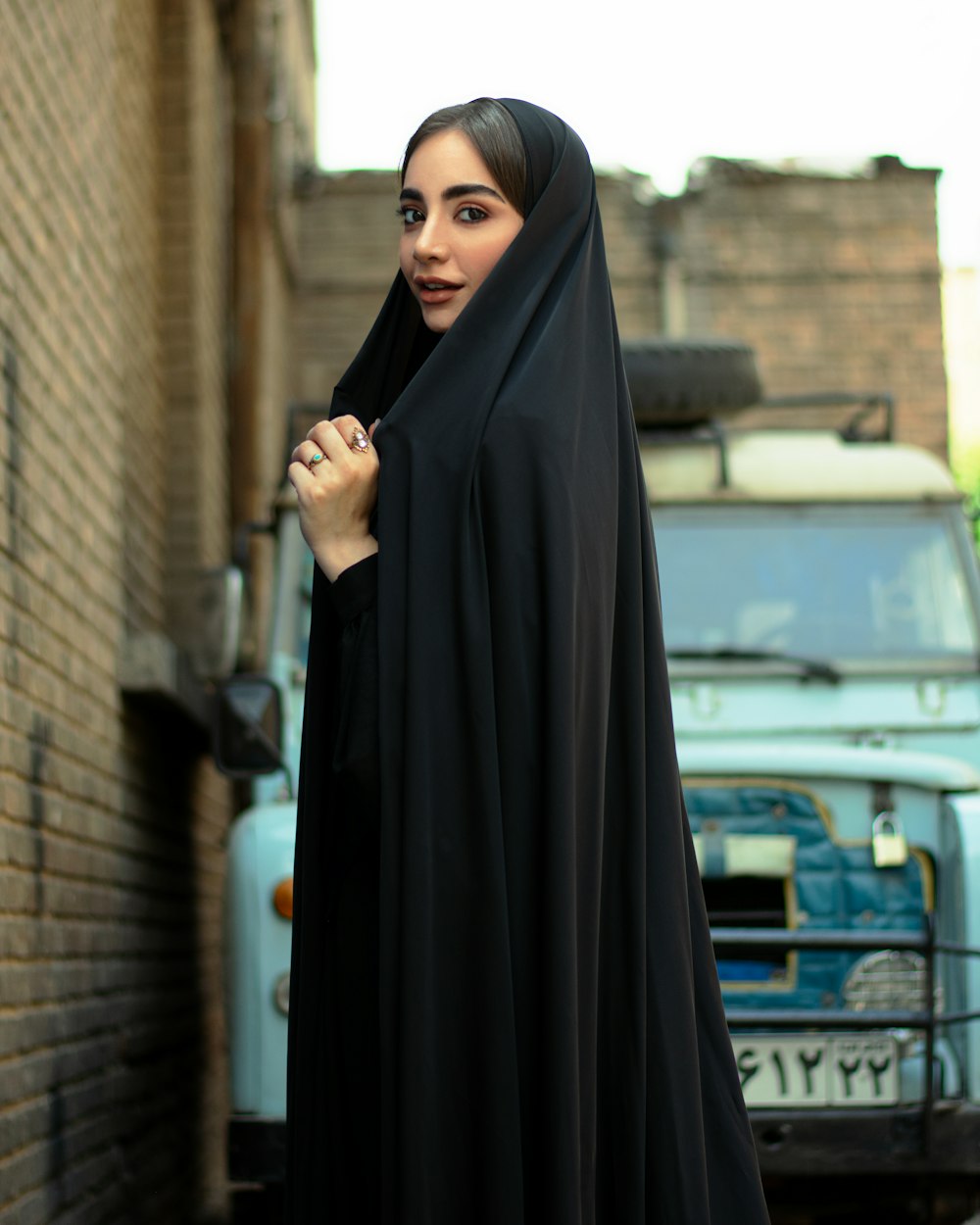 Frau im schwarzen Hijab steht tagsüber in der Nähe des Gebäudes
