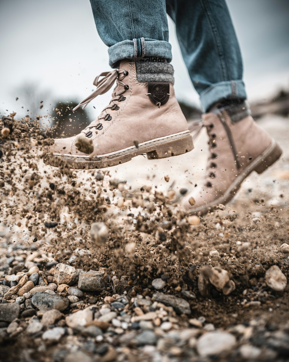 person in blue denim jeans and brown leather boots standing on rocky ground during daytime