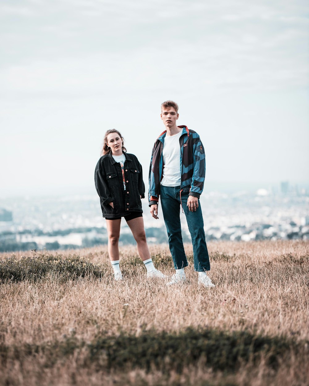 man in black jacket standing beside woman in blue jacket on brown grass field during daytime