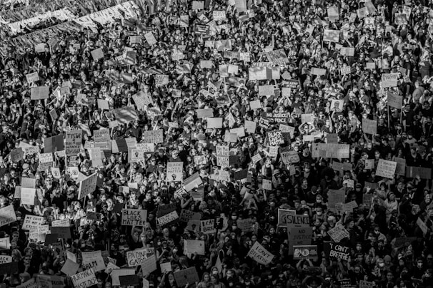 A large crowd of protesters holding various signs, many of which display messages related to social justice and equality. The image is in black and white, capturing the intensity and unity of the people gathered.