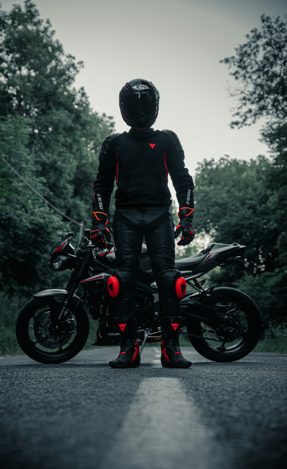 man in black jacket and blue denim jeans standing on black motorcycle during daytime