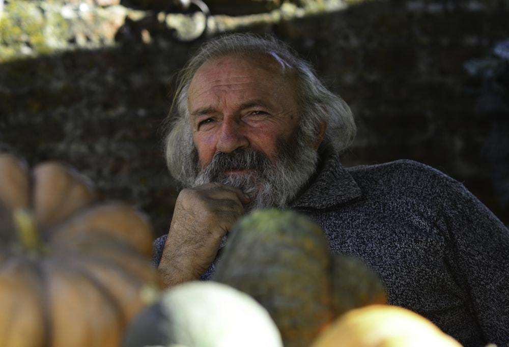 man in gray shirt with white beard surrounded by yellow and green round fruits