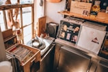 A cozy record store corner featuring a collection of vinyl records and a record player. Sunlight streams through a rustic window illuminating various items including albums with recognizable covers, a small speaker, and a cocktails menu. Shelves and bins are filled with records, creating a nostalgic atmosphere.