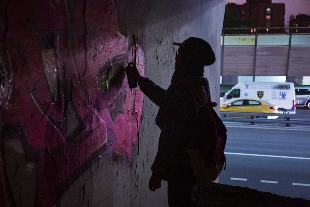 Hombre con chaqueta negra y pantalones negros de pie junto a la pared con graffiti durante el día