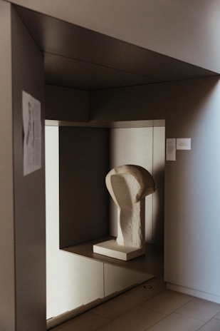 An elegant sculpture displayed on a minimalist white pedestal with soft lighting.