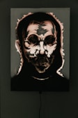 A dark and eerie portrait with abstract features, highlighting a skull-like face surrounded by shadows. The image appears to be accentuated by dramatic lighting and high contrast, emphasizing the harsh lines and textures