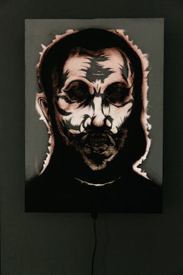 A dark and eerie portrait with abstract features, highlighting a skull-like face surrounded by shadows. The image appears to be accentuated by dramatic lighting and high contrast, emphasizing the harsh lines and textures