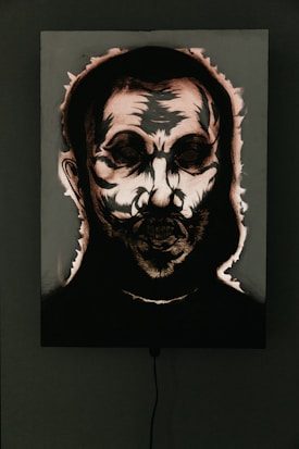 A dark and eerie portrait with abstract features, highlighting a skull-like face surrounded by shadows. The image appears to be accentuated by dramatic lighting and high contrast, emphasizing the harsh lines and textures