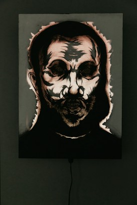 A dark and eerie portrait with abstract features, highlighting a skull-like face surrounded by shadows. The image appears to be accentuated by dramatic lighting and high contrast, emphasizing the harsh lines and textures