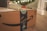 A cardboard box with Amazon branding sits on a wooden floor, with festive blue decorative tape featuring holiday motifs. In the background, a blurred image of a Christmas tree illuminated with lights can be seen, along with a few red and silver ornaments.