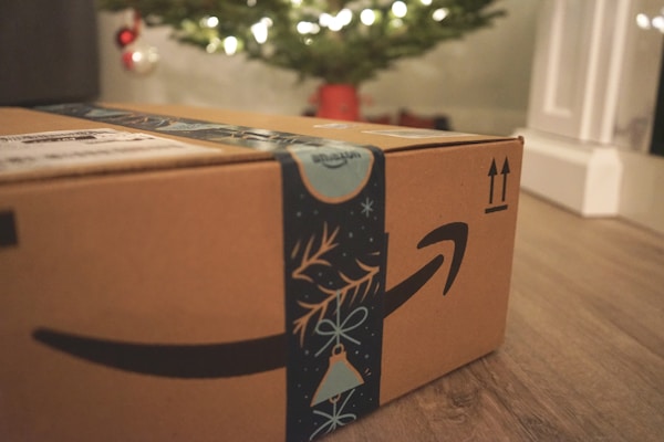Amazon delivery box with gifts in front of a Christmas tree.by Wicked Monday