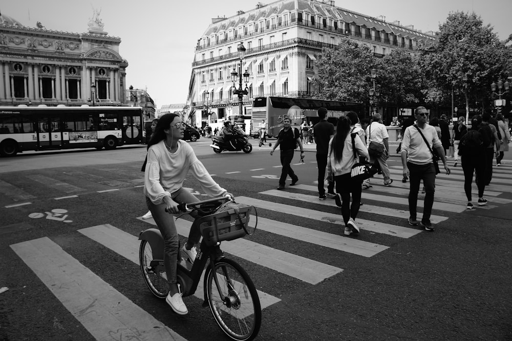 homem na camiseta branca que anda de bicicleta na faixa de pedestres na fotografia em tons de cinza