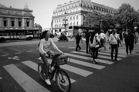 man in white t-shirt riding bicycle on pedestrian lane in grayscale photography in Palais Garnier France