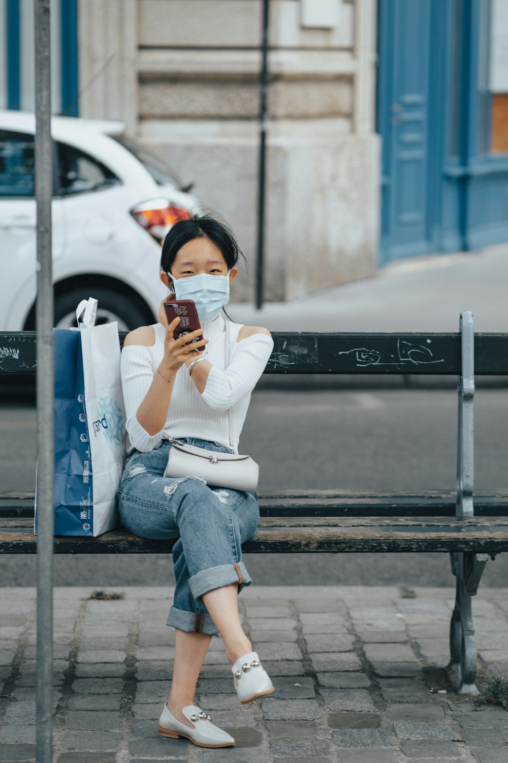 woman in white long sleeve shirt and blue denim jeans sitting on bench while holding white