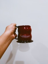 A hand holding a red mug with 'Radio Mirchi' printed on it against a plain background.