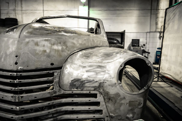 Artisan carefully layering fiberglass in a rustic workshop filled with vintage car parts.