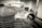 A vintage car is undergoing restoration in an industrial garage setting. The front of the car is stripped to bare metal, showing signs of sanding and preparation work. The environment is dimly lit with scattered tools and equipment visible in the background.