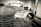 A vintage car is undergoing restoration in an industrial garage setting. The front of the car is stripped to bare metal, showing signs of sanding and preparation work. The environment is dimly lit with scattered tools and equipment visible in the background.
