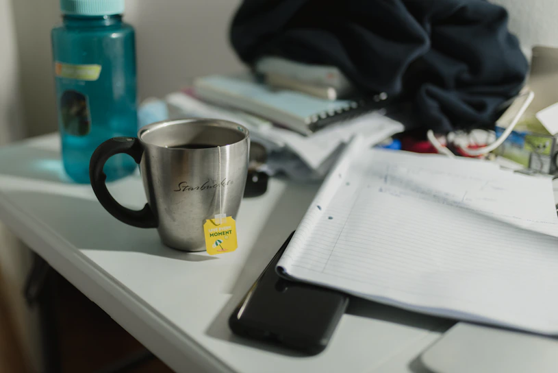 A cluttered desk with scattered notebooks, a half-eaten pork pie, and a steaming mug of tea, capturing the chaos of a busy mum's writing space.