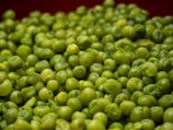 A close-up view of a pile of fresh green peas, with a smooth texture and a variety of shades of green.