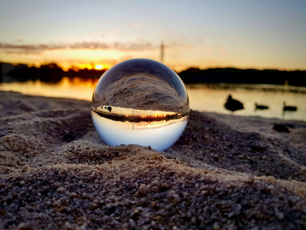 bola de vidrio transparente sobre arena marrón durante la puesta del sol