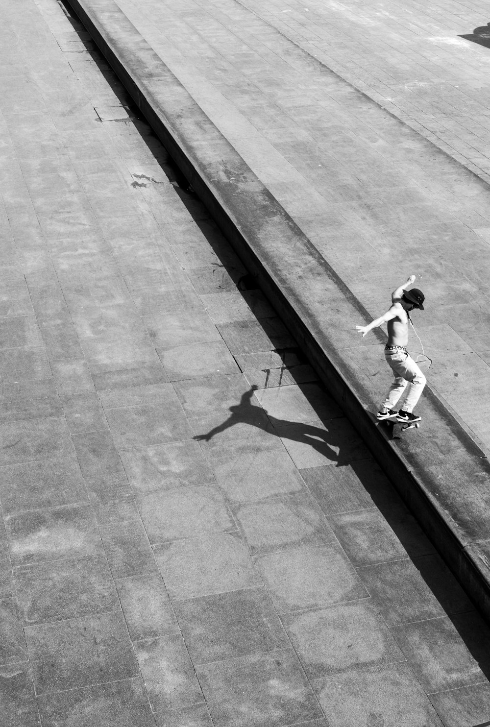 灰色のコンクリート舗装でスケートボードをする白いシャツとズボンの男
