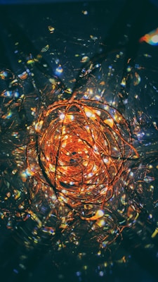 A cluster of intricate, glowing copper wires creates a mesmerizing spiral of lights. The warm, golden tones of the lights contrast with the dark, moody background, creating a vivid and dynamic visual experience.
